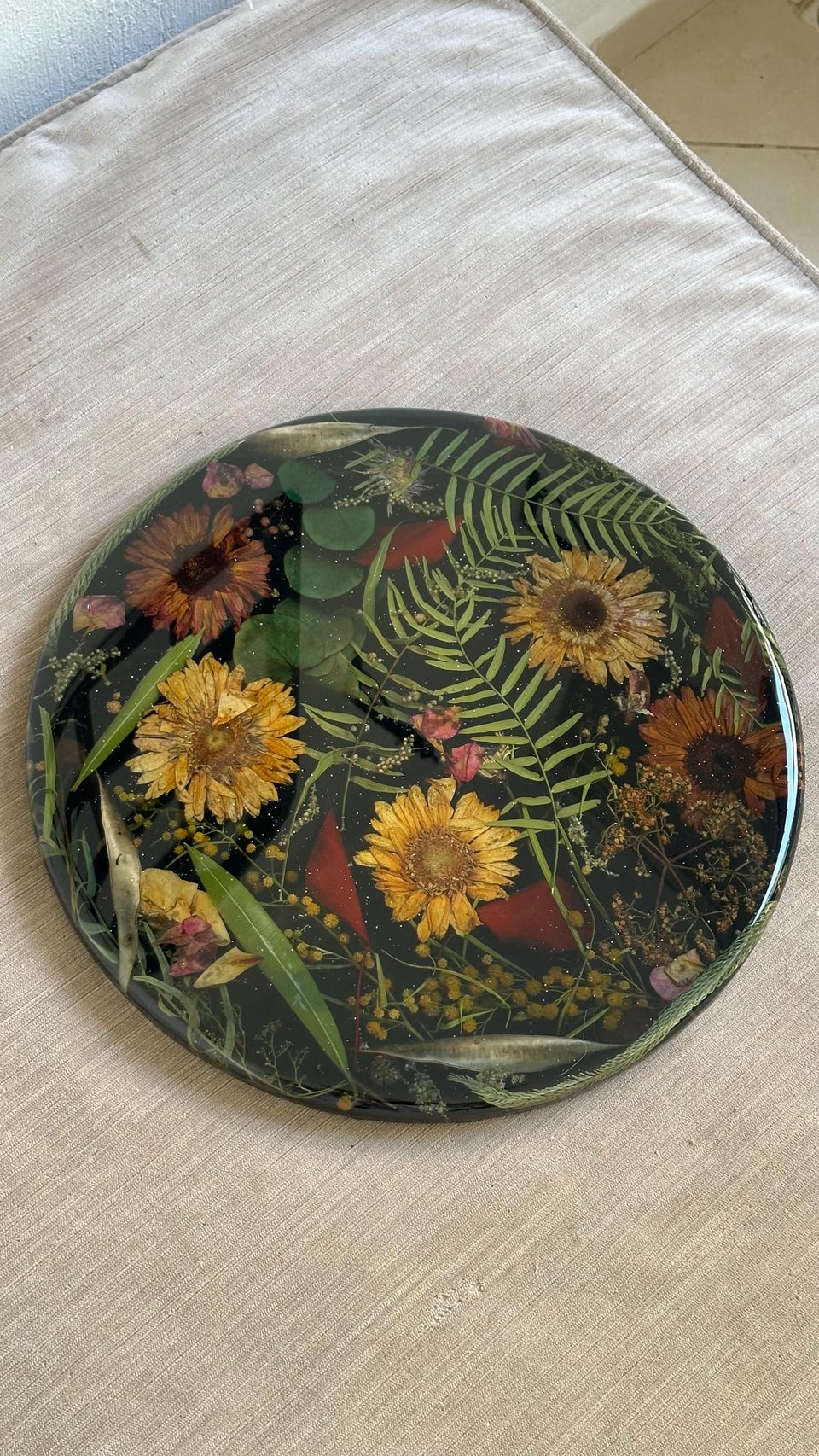 The black resin top seen from above: yellow and rust-colored dried flowers, ferns, eucalyptus leaves and red petals