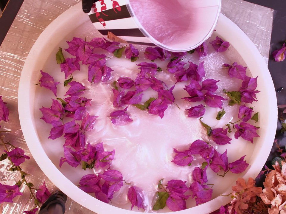 Milky pink resin poured from a cup over bougainvillea petals in a round mold