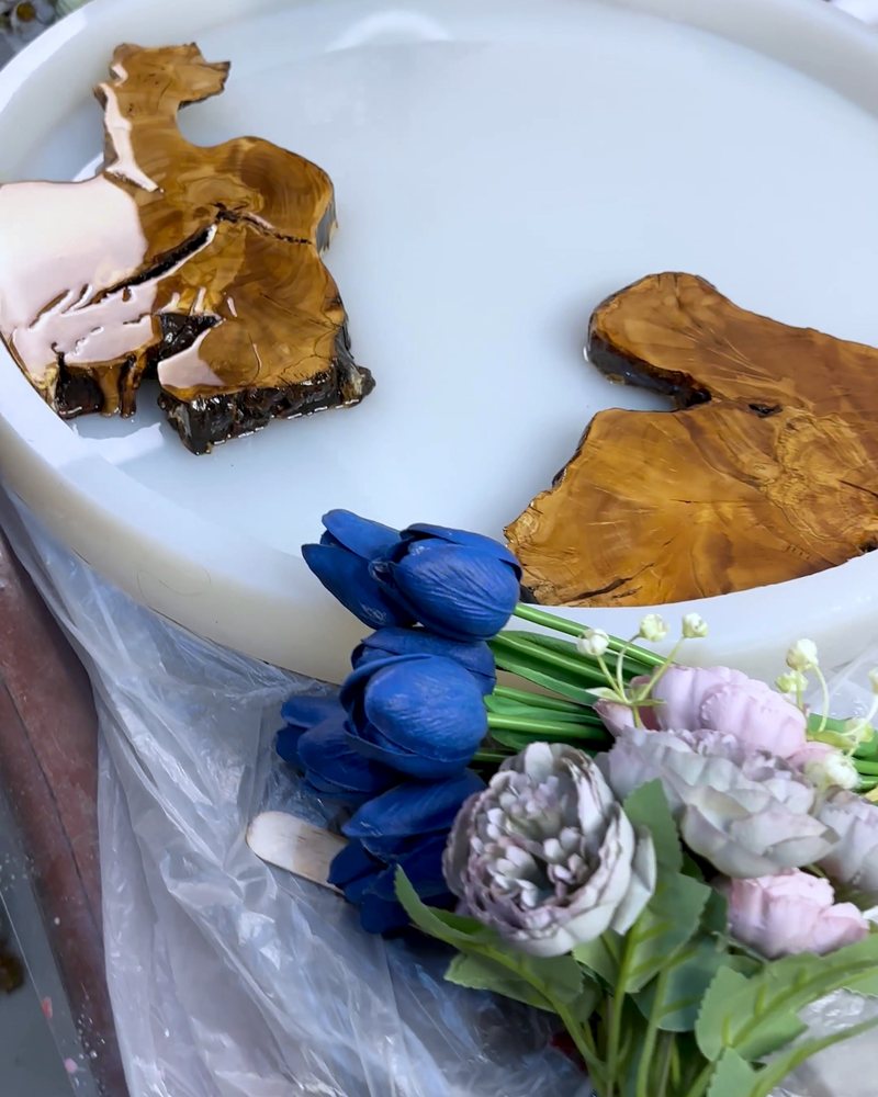 Pieces of olive wood laid in a round mold, with blue tulips and dried flowers beside it